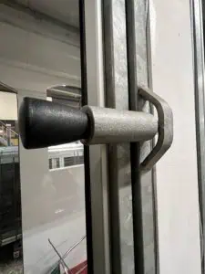 Närbild av en metallisk låsanordning med svart handtag vid en fönsterkarm